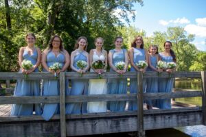 bride and bridesmaid posed on bridge in front of lake
