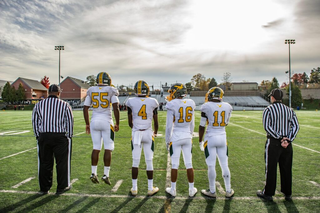 sports photo of four football players and two refs on the sideline